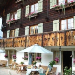 Vue rapprochée de la façade en bois sombre du chalet, fenêtres fleuries de géraniums