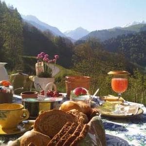 Petit-déjeuner servi en terrasse — café, pain, confitures et jus avec les montagnes en arrière-plan
